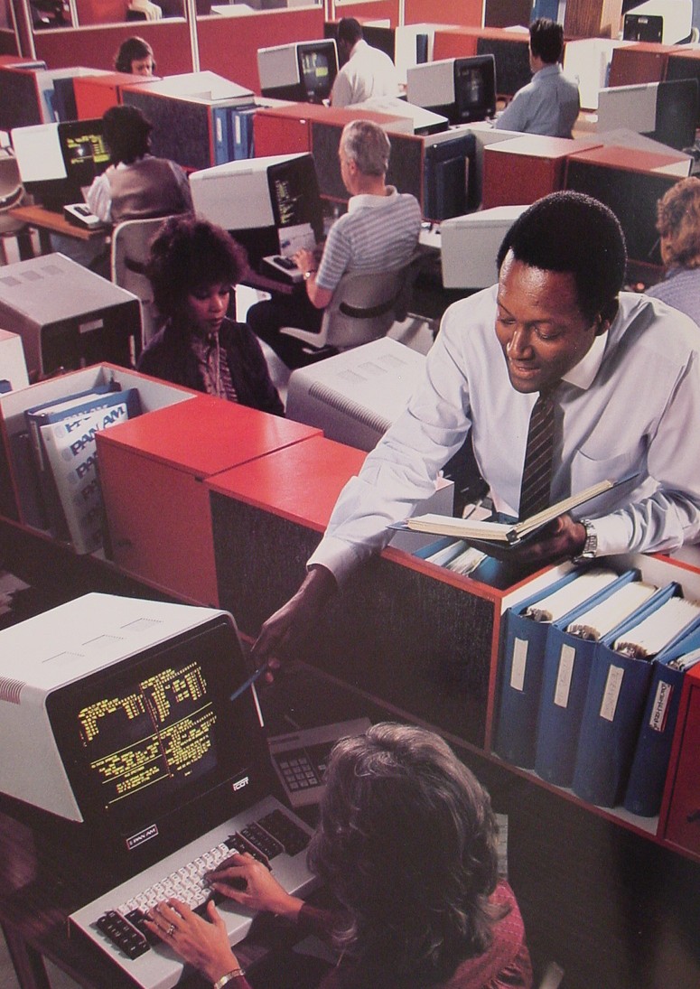 1980s A reservations trainer assists an agent with a computer transaction.
